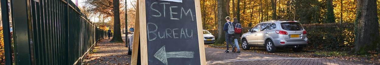 Straatbeeld met bord waarop in krijt staat geschreven: 'Stembureau'.