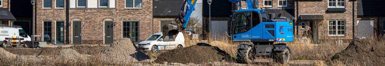 Een blauwe graafmachine graaft grond af in een nieuwbouwwijk