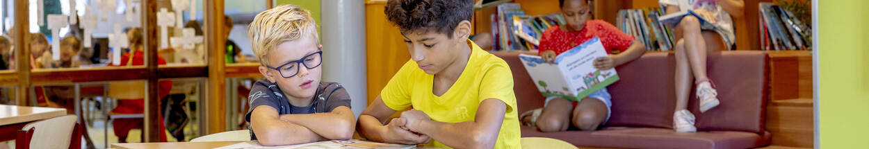 Foto van basisschoolkinderen die boeken lezen in de bibliotheek